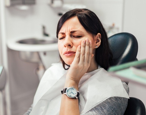 Woman holding cheek before receiving emergency dentistry