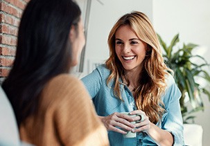 Woman smiling while drinking coffee with friend