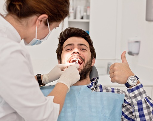 A young man giving a thumbs up while receiving a dental checkup