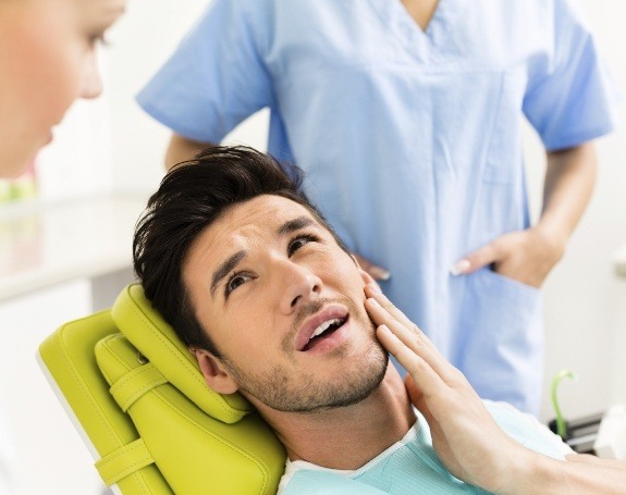 Man experiencing common dental emergencies holding jaw in pain