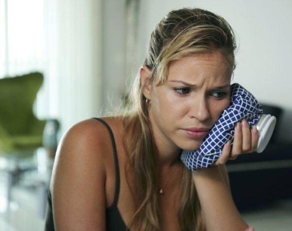 Woman in need of emergency dentistry holding ice pack to cheek