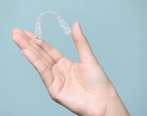 Patient holding clear aligner against blue background